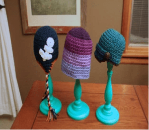 Three crocheted hats on a green stand.